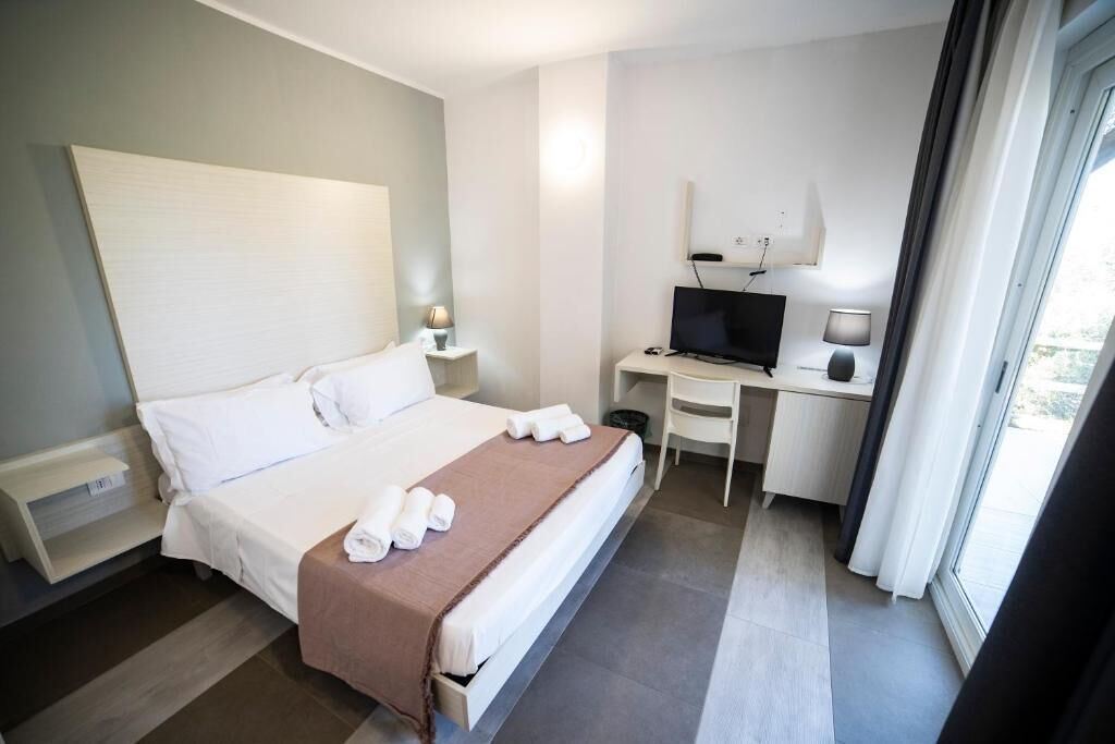 Habitación de hotel con cama, escritorio con computadora, televisor y ventana.
