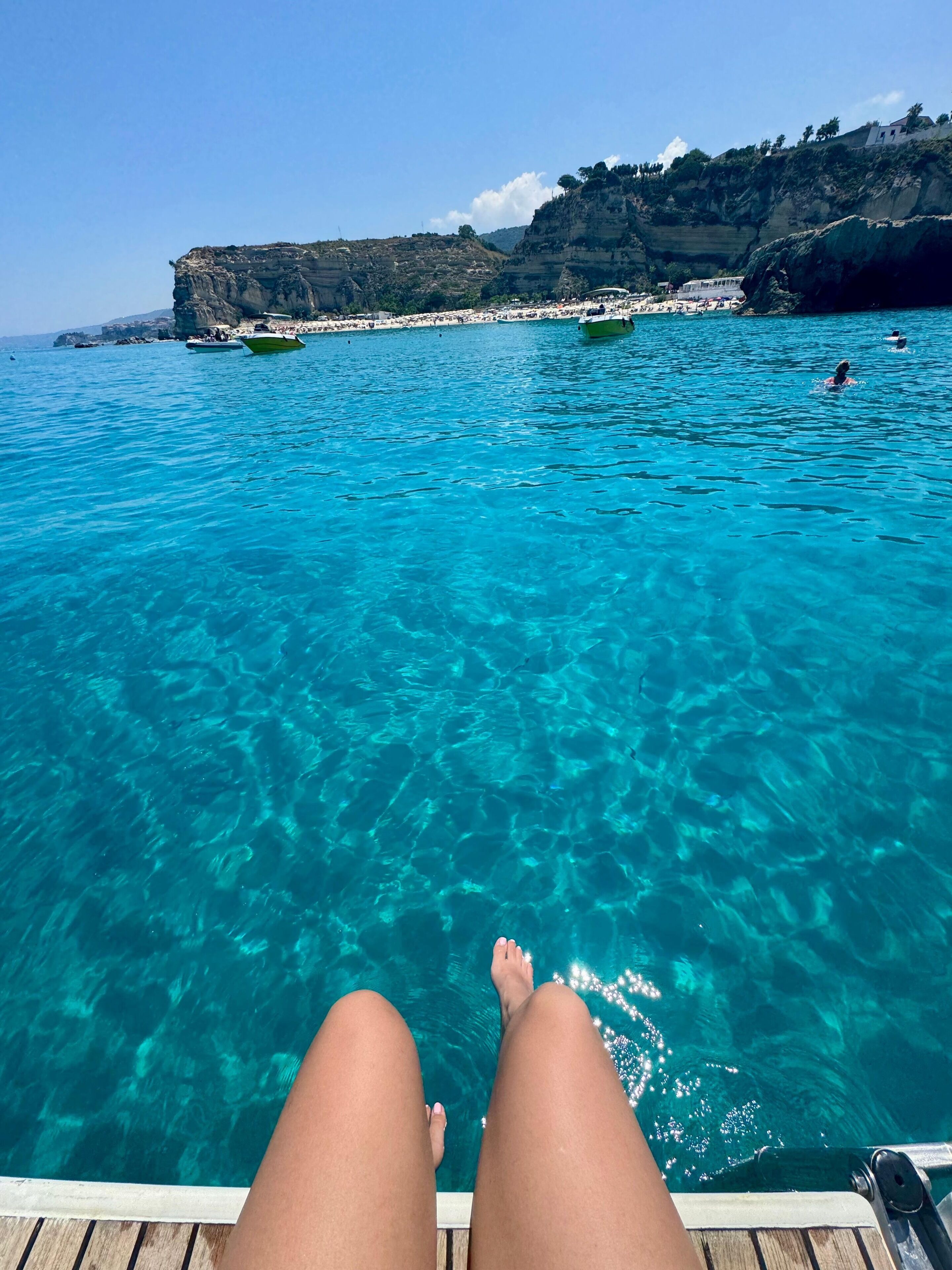 Vista nítida de um cais de madeira que se estende por um mar azul-turquesa, com falésias rochosas ao fundo.