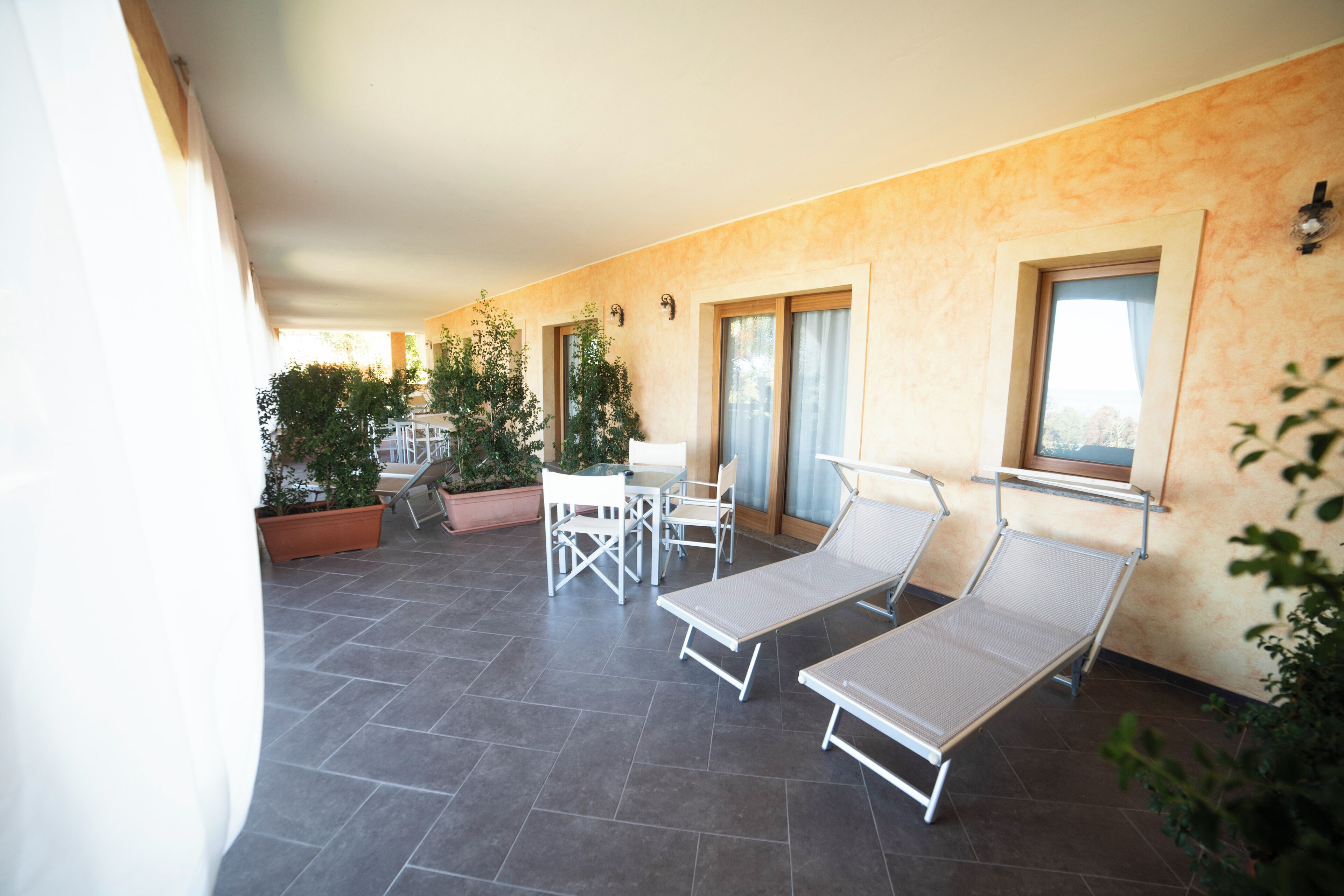 A sunlit patio with a table and chairs, lounge chairs, and potted plants.