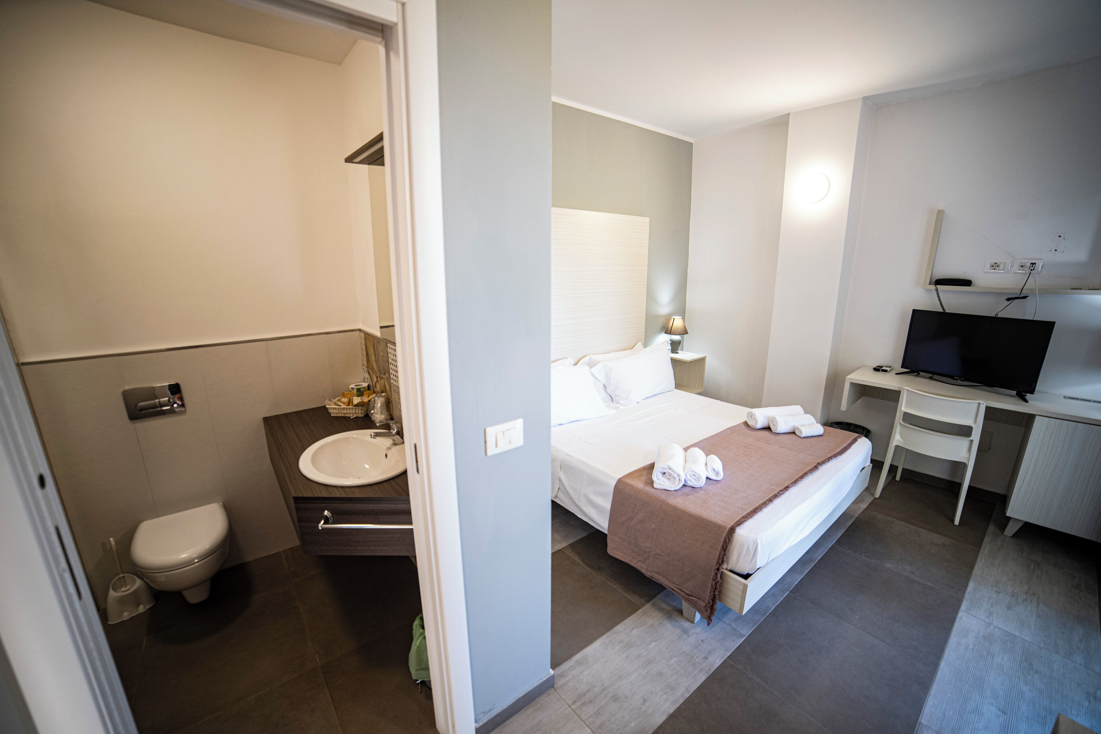 Une chambre d’hôtel comprenant un lit, un bureau avec un ordinateur, une télévision et une salle de bain avec des toilettes et un lavabo.