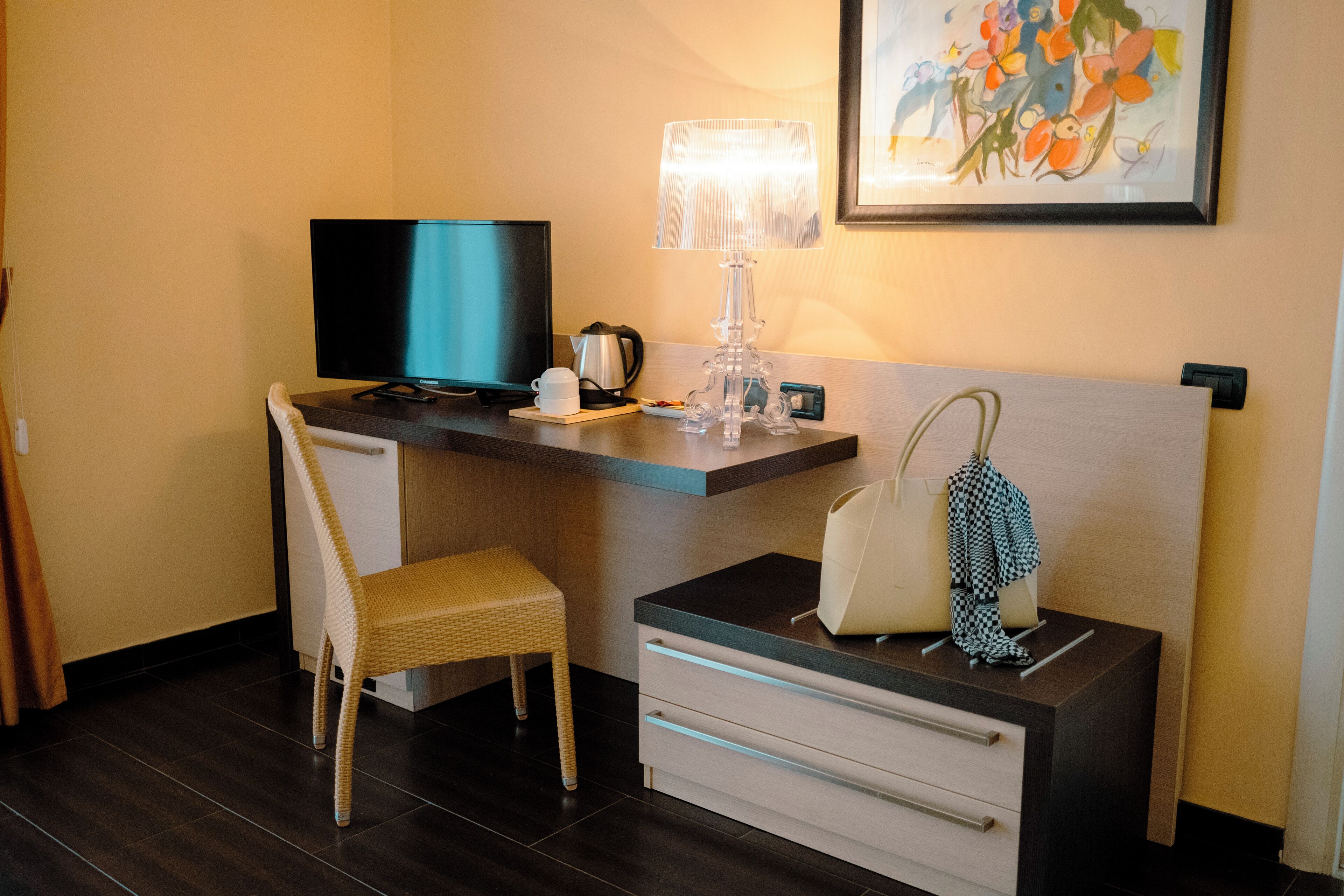 A hotel room with a desk, chair, television, lamp, and a painting on the wall.
