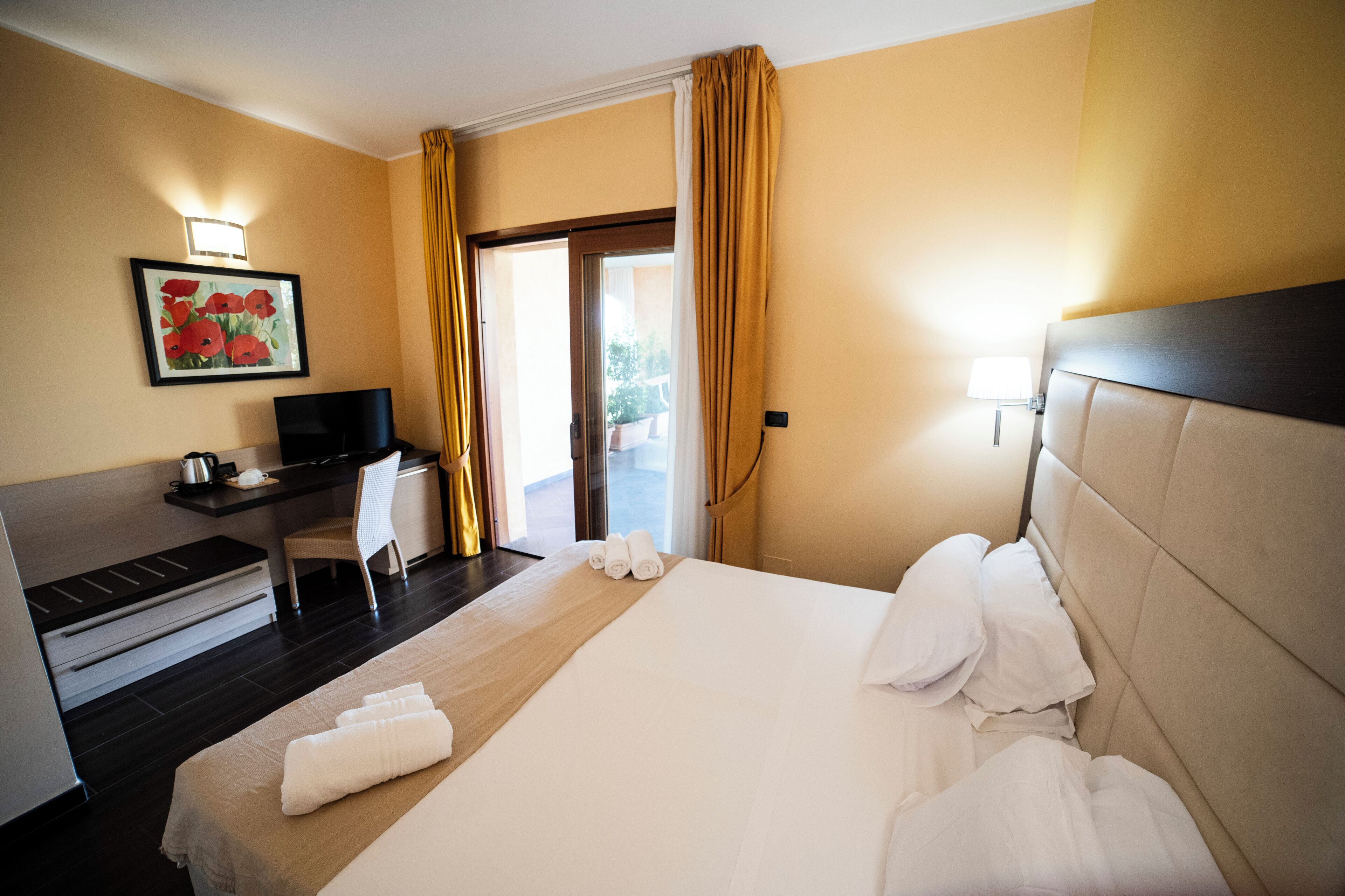 Een hotelkamer met een bed, een bureau, een televisie en een schilderij aan de muur.