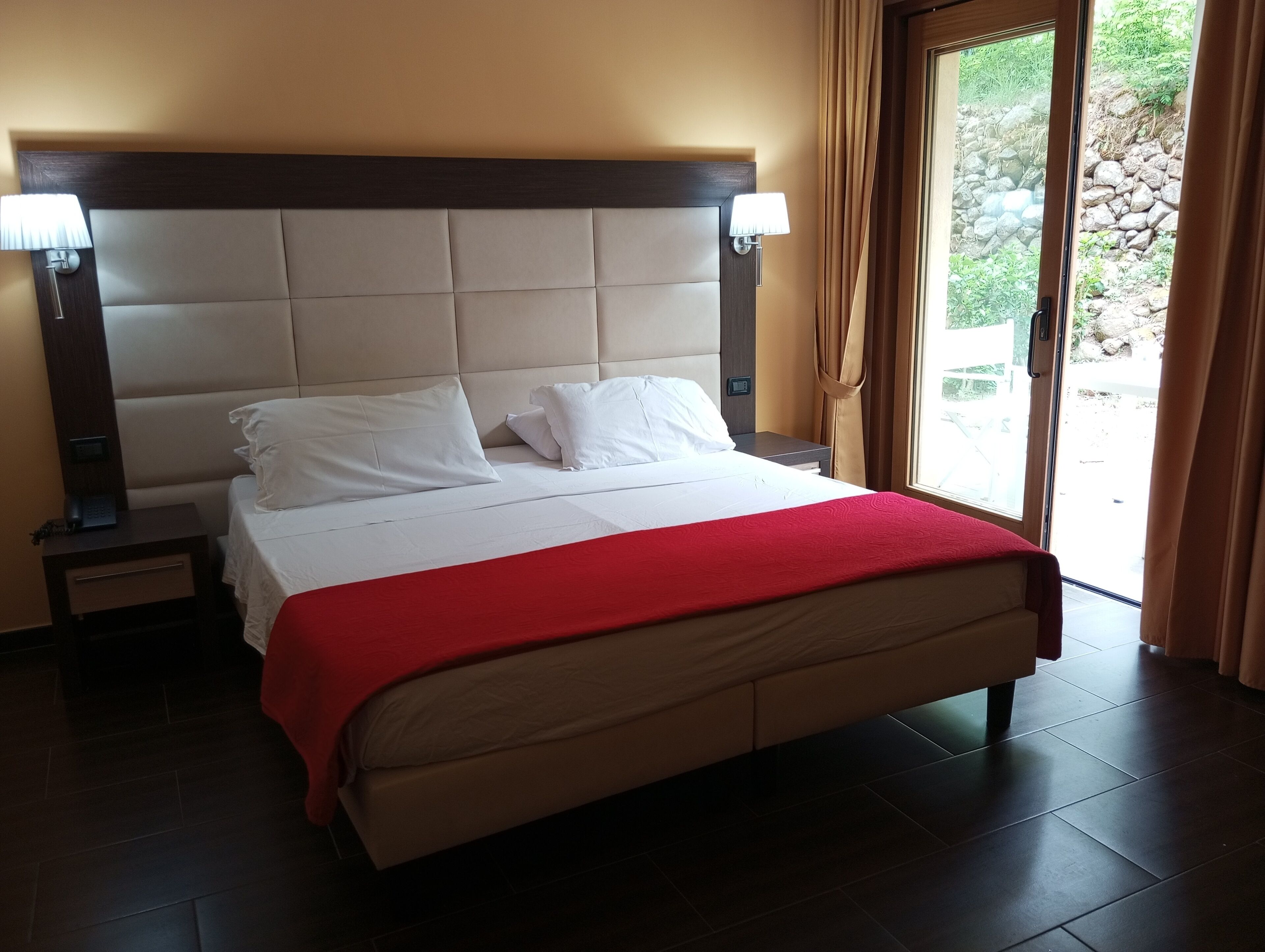 Ein Hotelzimmer mit einem großen Bett, zwei Nachttischen und Blick ins Freie.