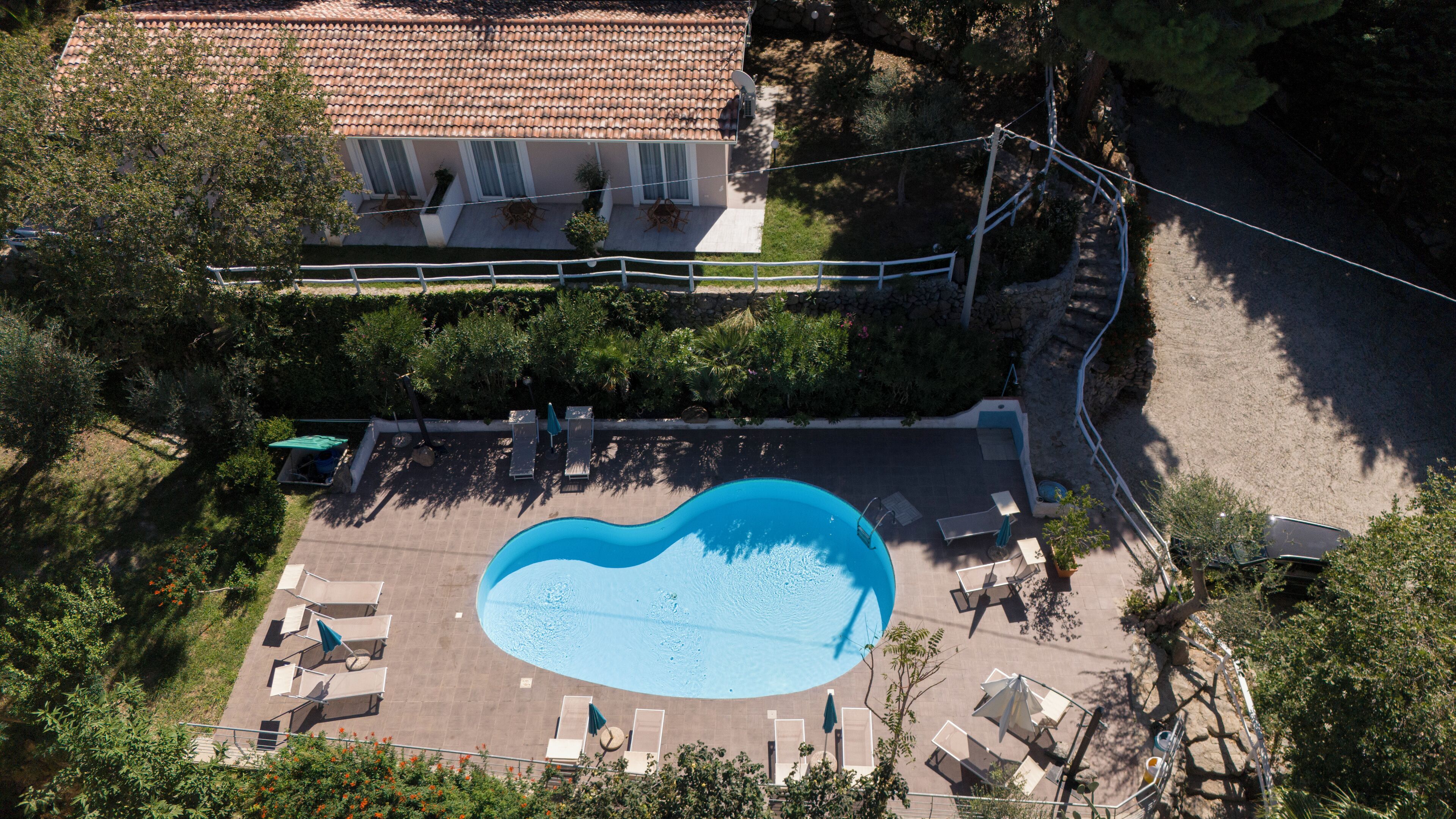 An aerial view of a residential property with a swimming pool, lounge chairs, and a house with a tiled roof.