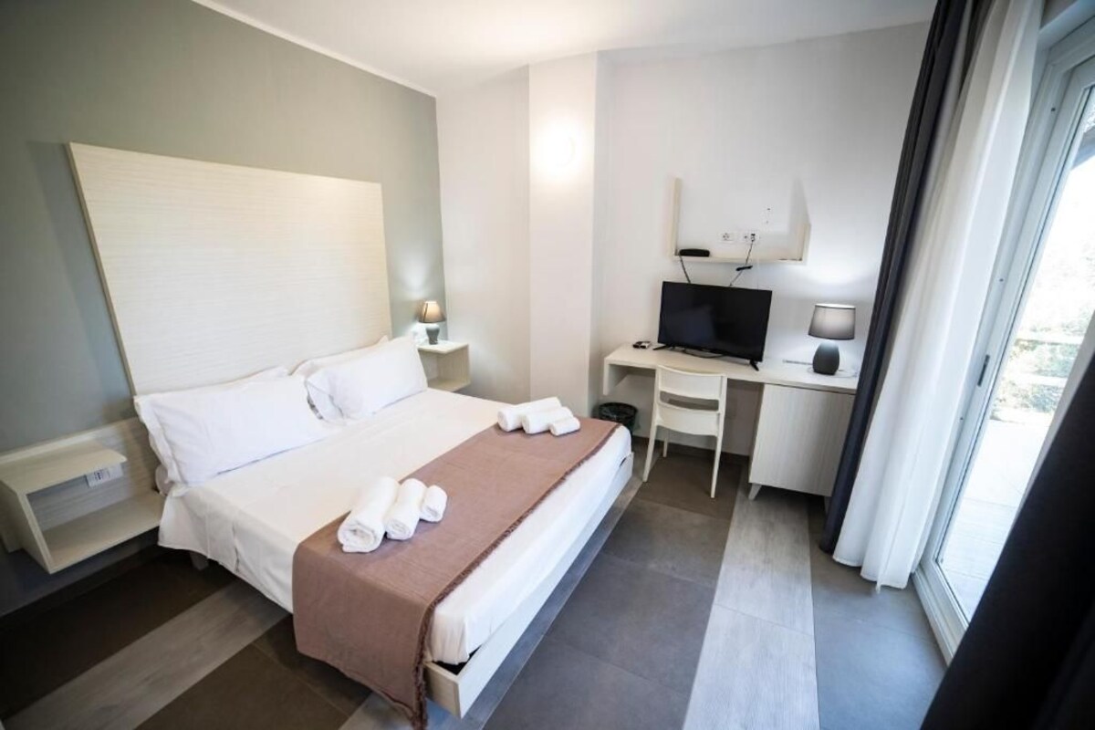 A hotel room with a bed, a desk with a computer, a TV, and a window.