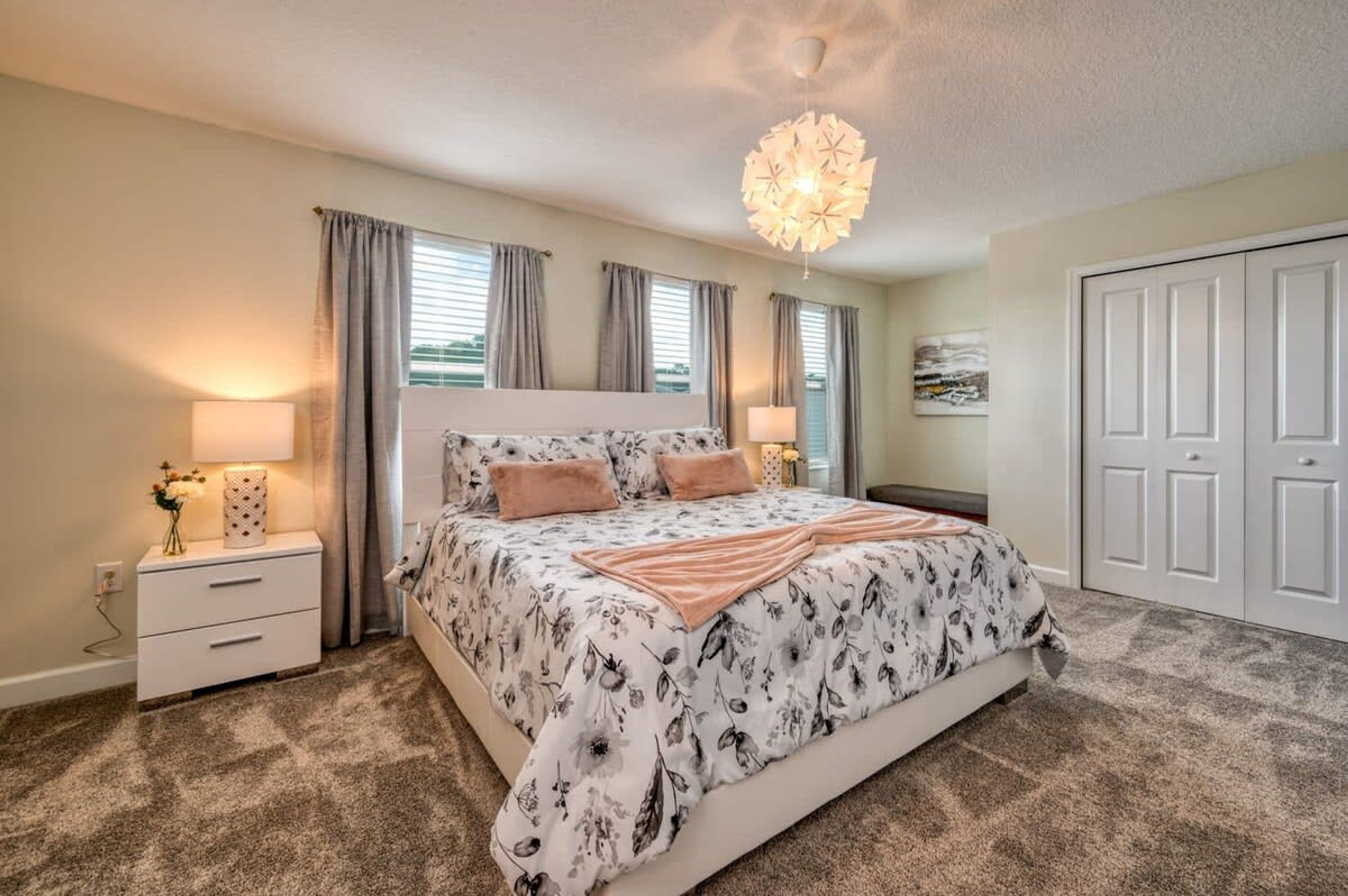 A bedroom with a large bed, two bedside tables with lamps, a ceiling light fixture, and a wardrobe.