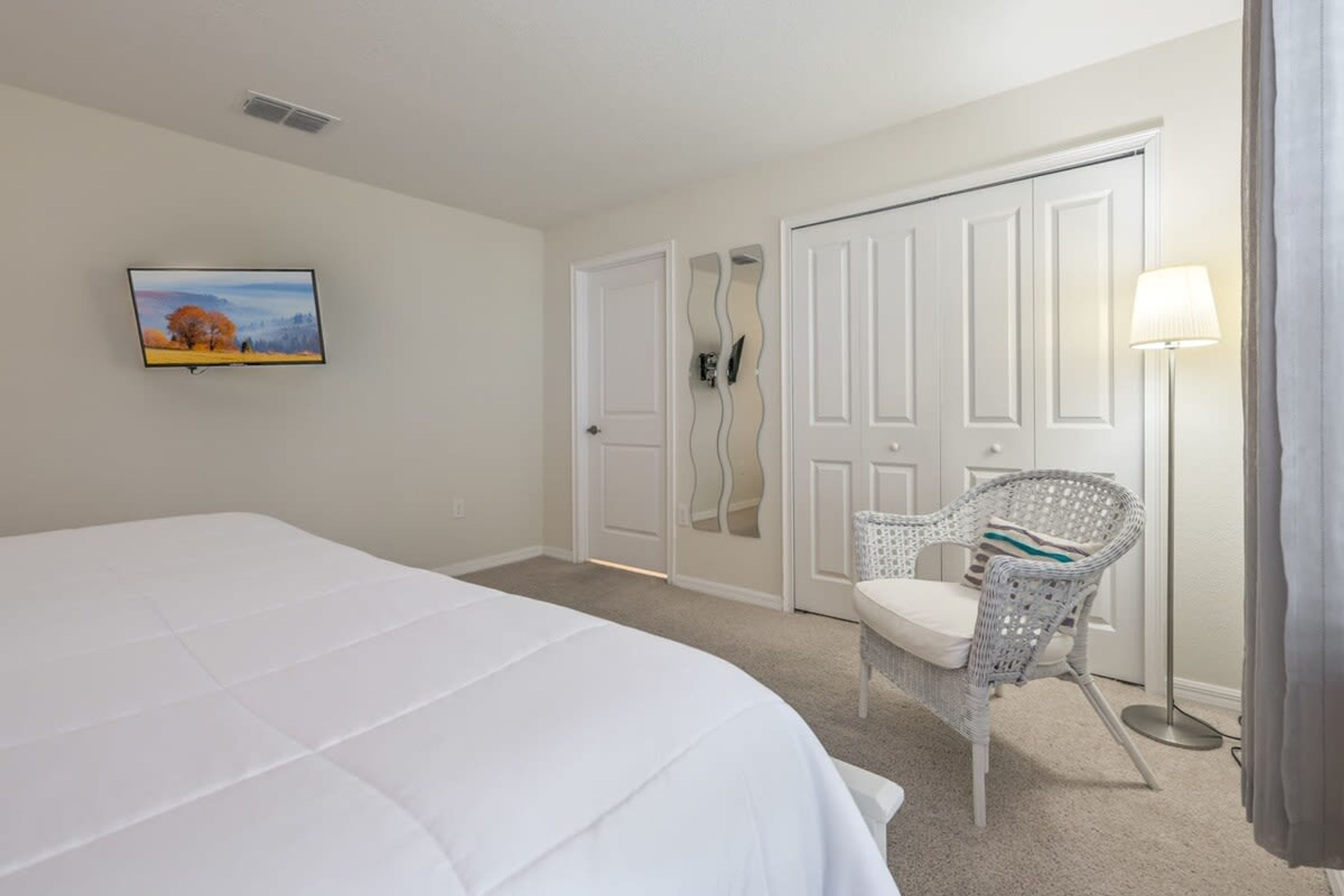 A hotel room with a bed, a chair, a television, and a door with a mirror.