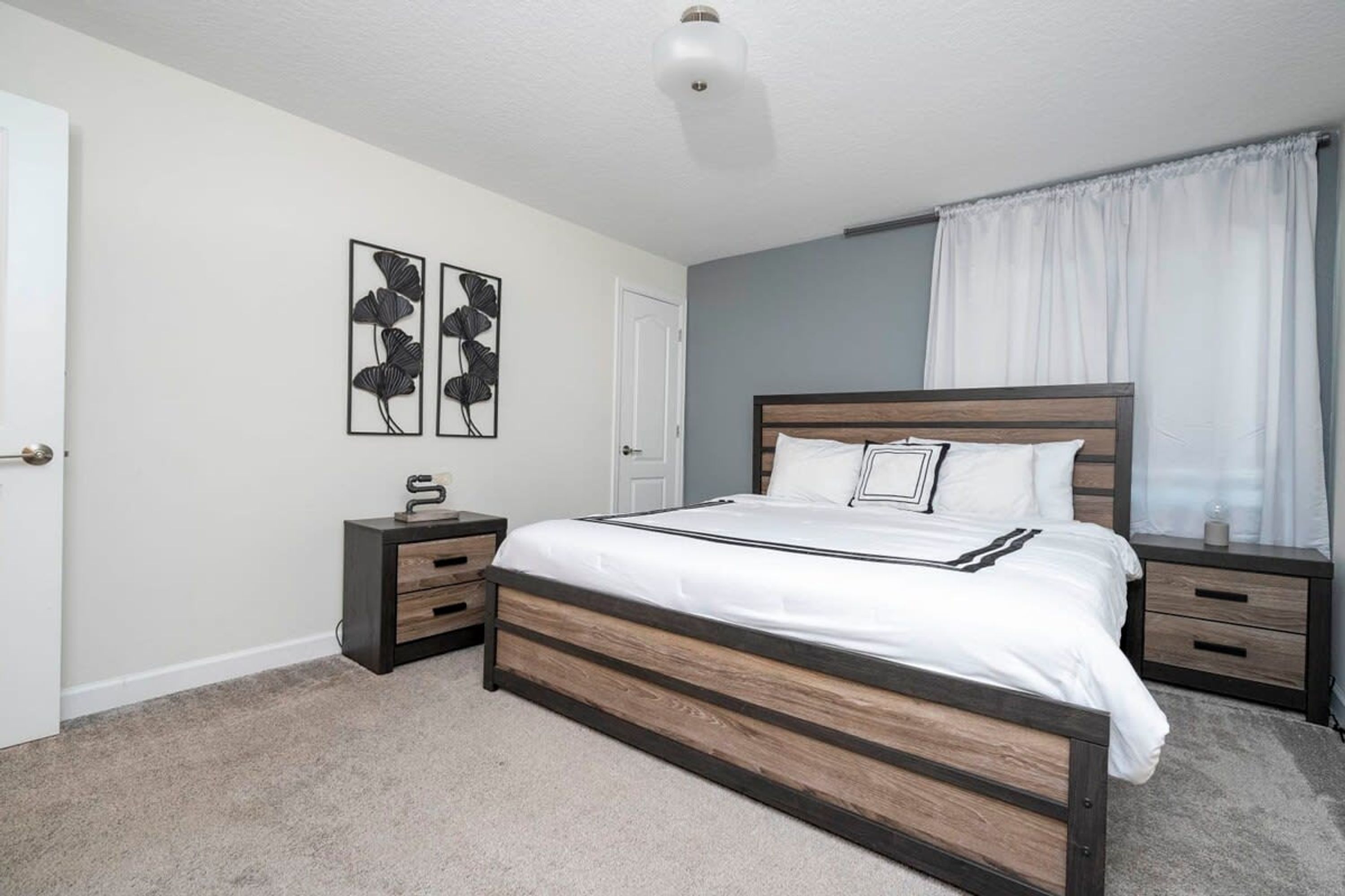 A bedroom with a wooden bed frame, white bedding, two bedside tables, and wall art.