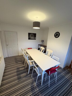 A room with a white table, white chairs, a black clock, a lamp, and a door. - "Central Skipton Townhouse • Sleeps 10 • Walk to Everything • Free Parking (Skipton)