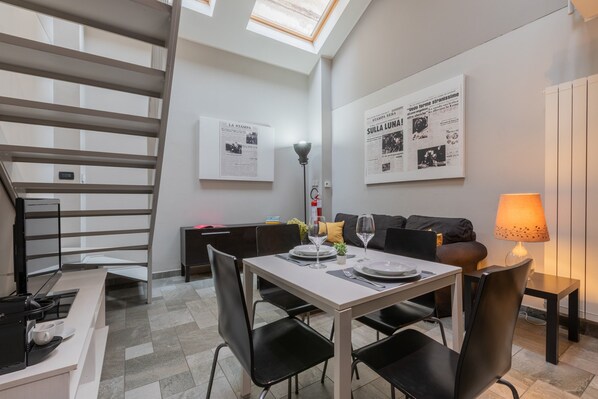 A modern dining area with a table set for two, a sofa, and a staircase. - Loft Stampa by Wonderful Italy (Turin)
