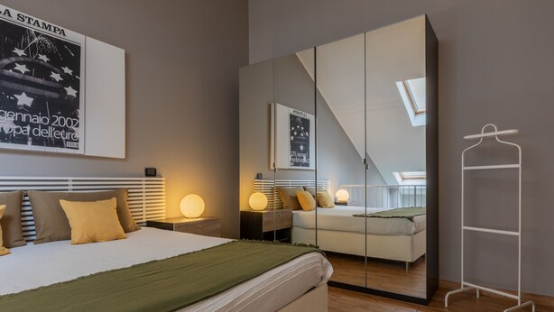 A modern bedroom with a large bed, bedside tables with lamps, a wardrobe, and a mirror. - Loft Stampa by Wonderful Italy (Turin)
