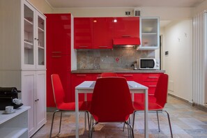 A compact kitchen with red cabinets, a microwave, and a white table with red chairs. - Loft Vermouth by Wonderful Italy (Turin)
