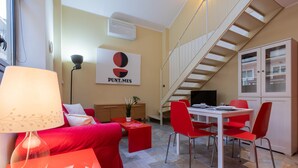 Una sala de estar moderna con un sofá rojo, una mesa de comedor con sillas rojas, una escalera y un armario con puertas de vidrio.