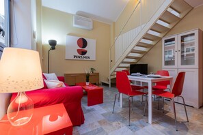 A modern living room with a red sofa, a dining table with red chairs, a staircase, and a cabinet with glass doors. - Loft Vermouth by Wonderful Italy (Turin)