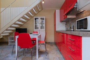 A compact kitchen with red cabinets, a microwave, and a dining area with red chairs and a white table. - Loft Vermouth by Wonderful Italy (Turin)