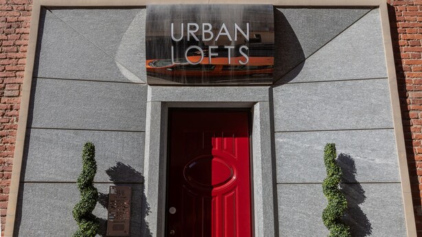 Entrada de un edificio con un letrero que dice 'URBAN LOFTS' y una puerta roja.