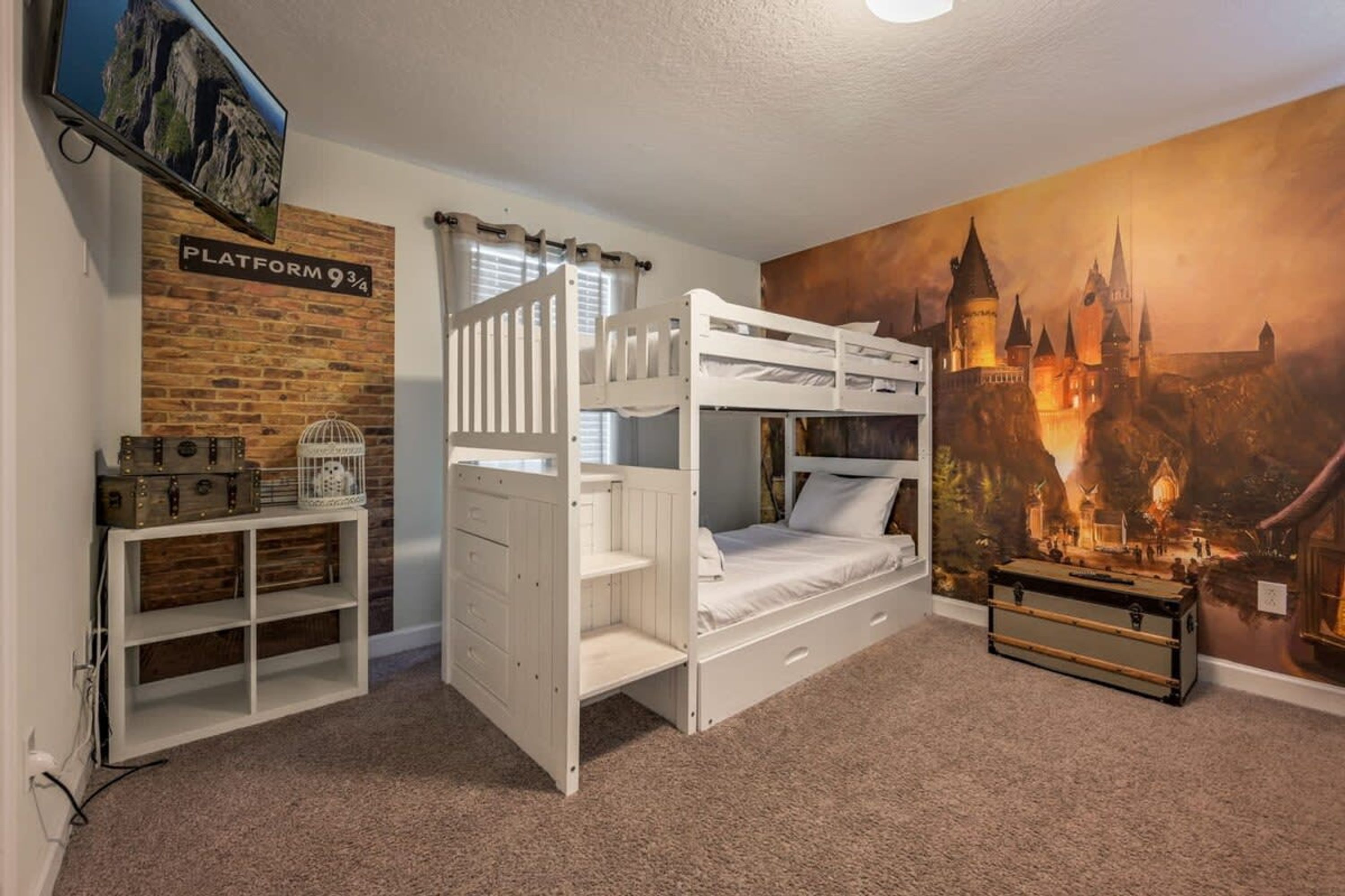 A bunk bed room with a brick wall, a mounted TV, and a castle-themed mural.