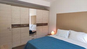 Een slaapkamer met een bed, nachtkastje, lamp en een garderobe.