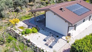 Een huis met een dak voorzien van zonnepanelen, een overdekt terras en een pad van stenen dat naar de ingang leidt.