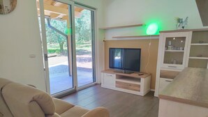 Een woonkamer met een bank, een televisie op een houten meubel, een schuifpui naar buiten en een kast met glazen deuren.
