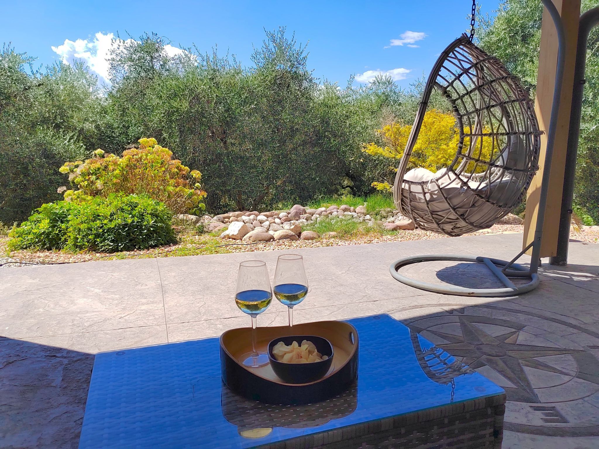 Eine Terrasse mit einer Hängematte, einem Tisch mit einer Schale Snacks und zwei Weingläsern, und einem dekorativen Kompassmuster auf dem Boden.