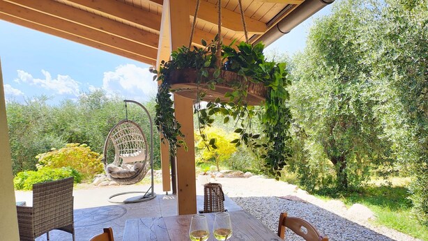 Een buitenterras met een houten tafel, stoelen, een hangstoel en een hangplanter.
