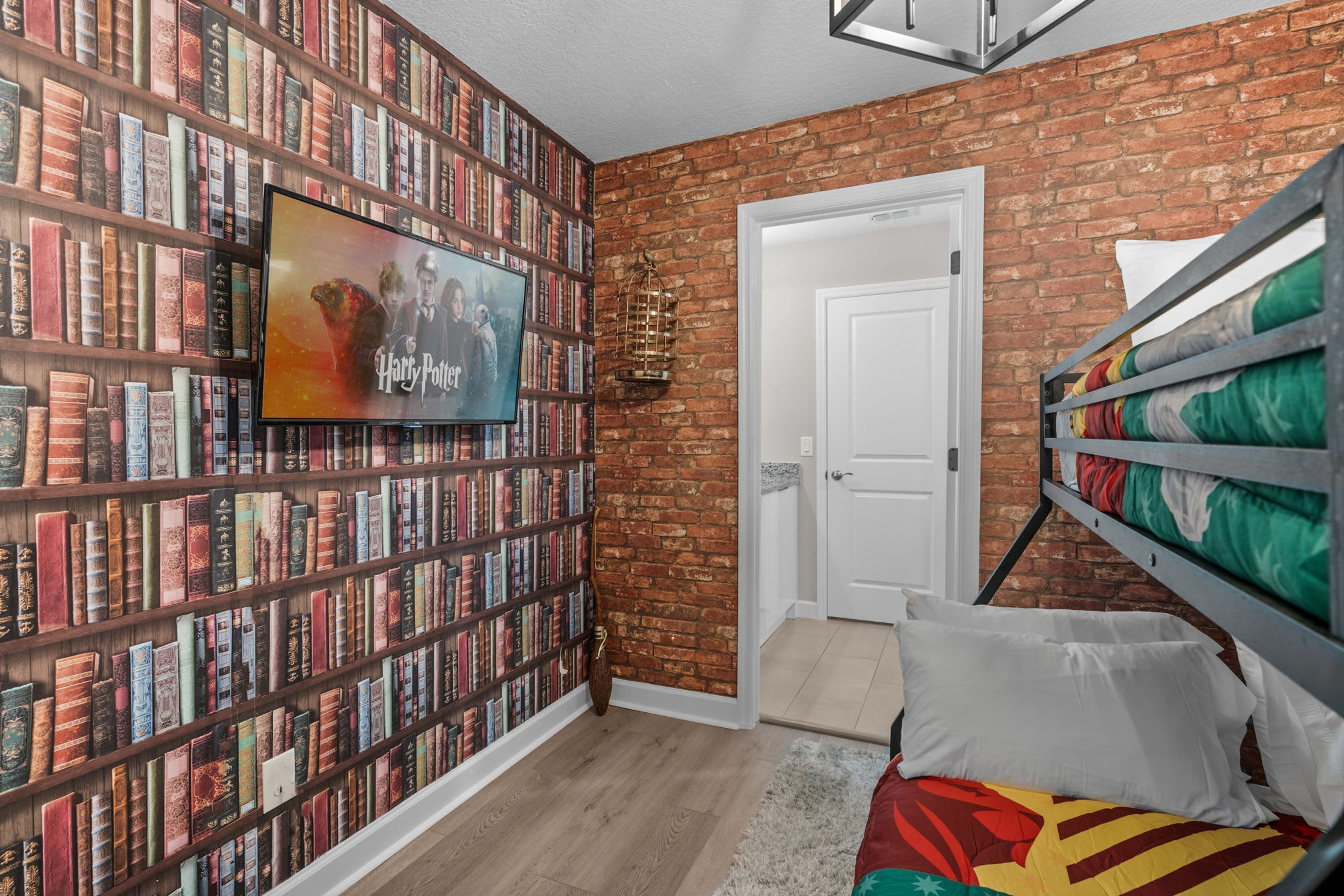 A room with a brick wall, a bookshelf filled with books, a TV mounted on the wall, and a bunk bed with colorful bedding.