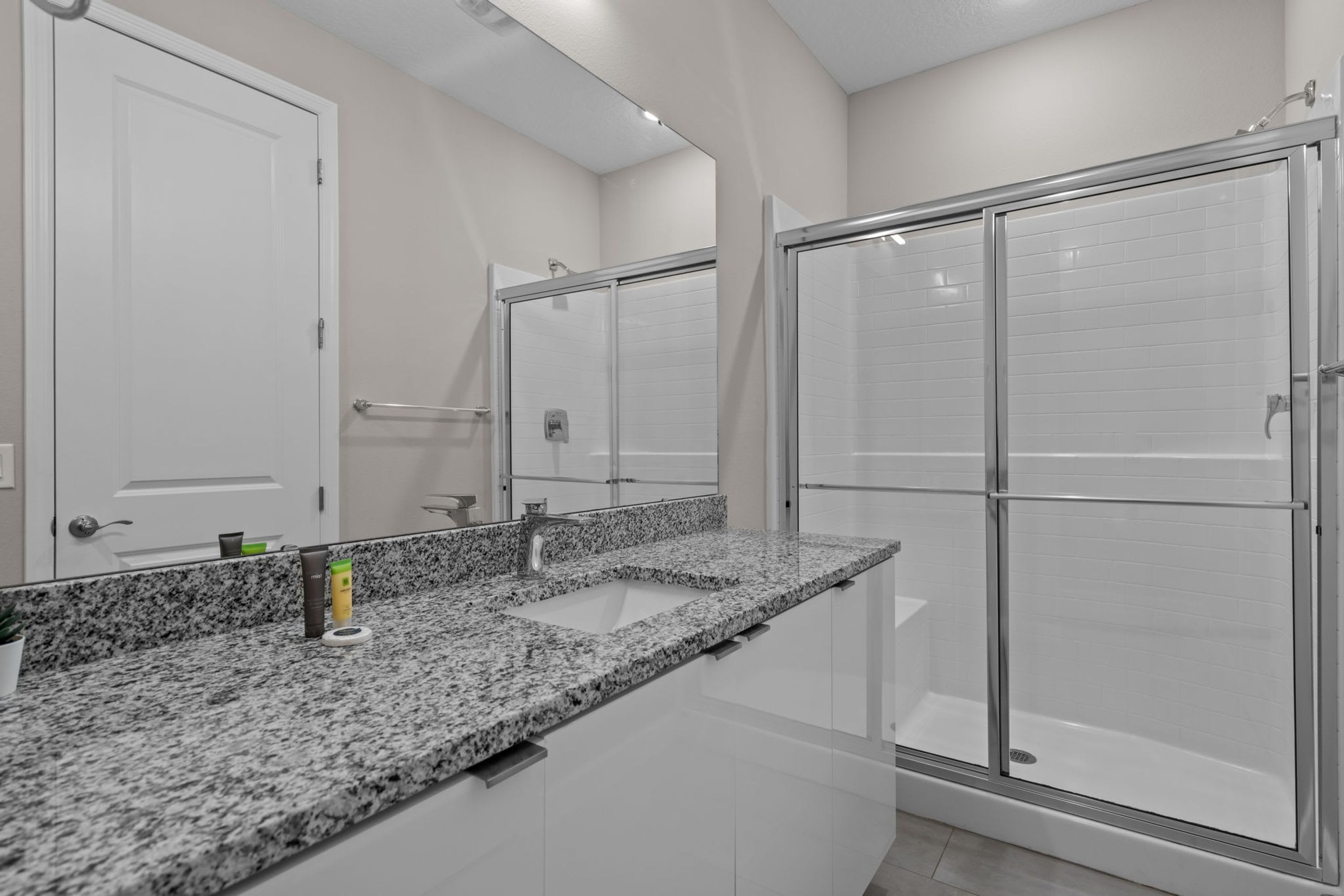A modern bathroom with a granite countertop, a sink, a mirror, and a glass-enclosed shower.