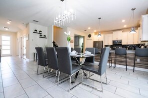 A modern kitchen with stainless steel appliances, a dining area with a chandelier, and a view of the living room. - Modern Marvel-Spacious, Themed, Fun-Filled Family Getaway (Kissimmee)
