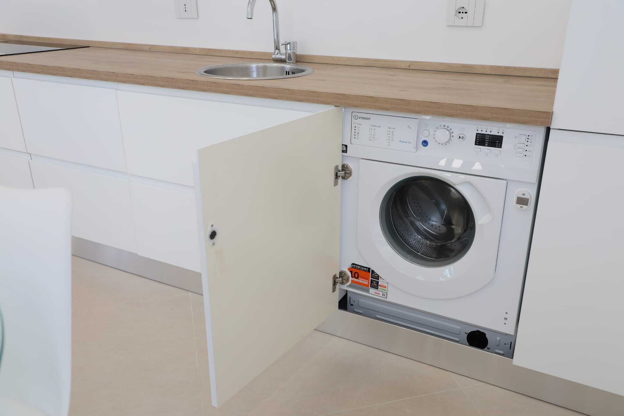 A compact kitchen with a built-in washing machine, a sink, and a wooden countertop.