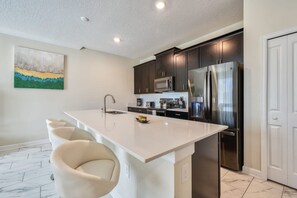 A modern kitchen with dark cabinets, stainless steel appliances, and a white island with bar stools. - Tranquil Retreat - Serene Getaway (Four Corners)