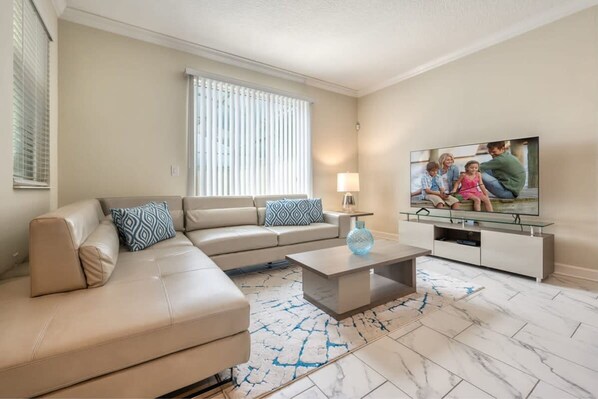 Ein Wohnzimmer mit einem beigefarbenen Sofa, einem Glastisch und einem Fernseher auf einem Lowboard.
