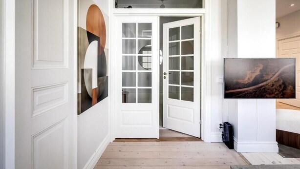 Un pasillo con paredes blancas, piso de madera y una puerta con paneles de vidrio.