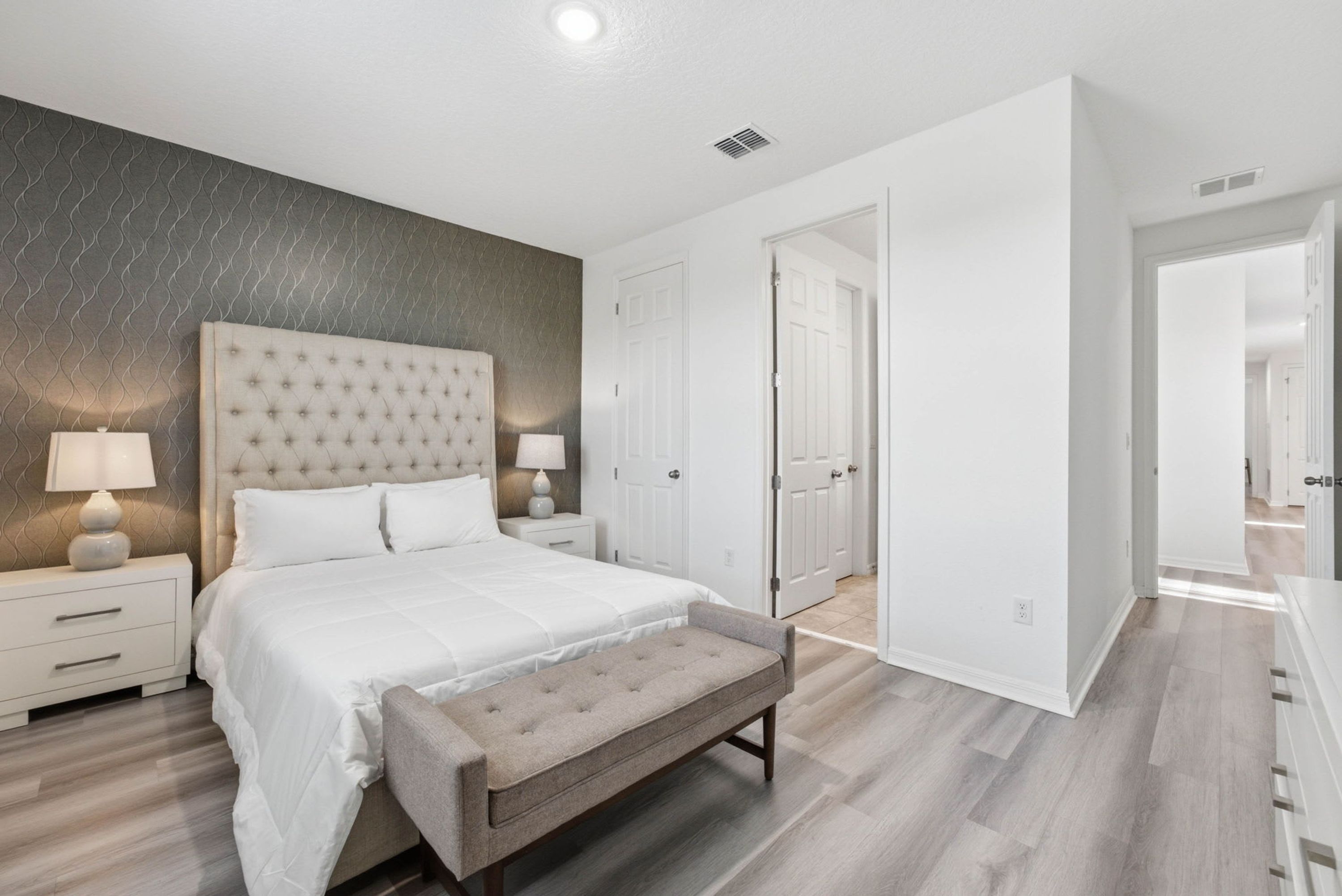 A bedroom with a large bed, bedside tables, a bench, and a wardrobe.