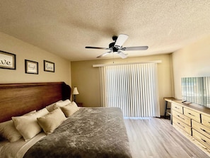 Ein Schlafzimmer mit Bett, Deckenventilator, Nachttisch, Lampe, Kommode und Fernseher.