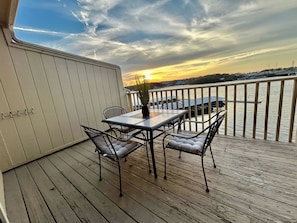 Eine Terrasse mit Tisch und Stühlen, die auf ein Gewässer mit Sonnenuntergang Blick blickt.