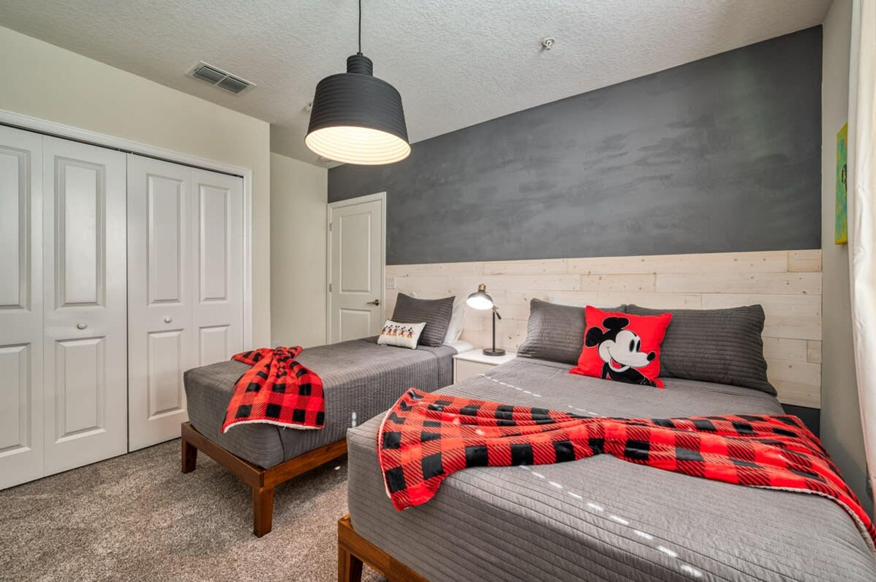 A bedroom with two beds, a headboard, a nightstand, a lamp, and a closet.