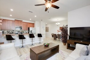 A modern living room with a TV, sofa, coffee table, and a dining area with chairs. - Private Pool, Prime Location, Beautiful Home (Kissimmee)
