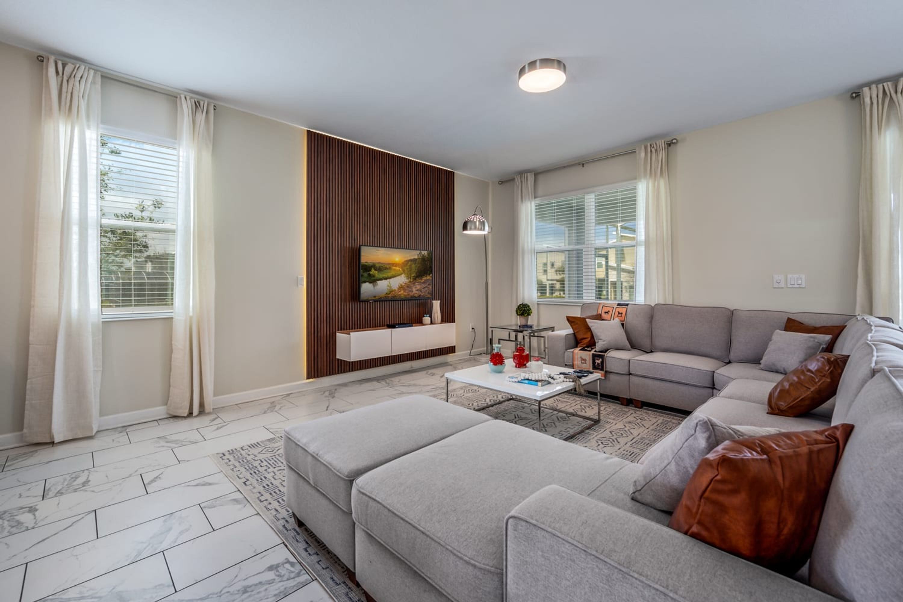 A modern living room with a sectional sofa, a coffee table, and a flat-screen TV mounted on a wooden panel wall.