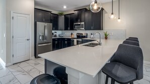 Een moderne keuken met donkere kastjes, roestvrijstalen apparatuur, een wit kookeiland en hangende verlichting.