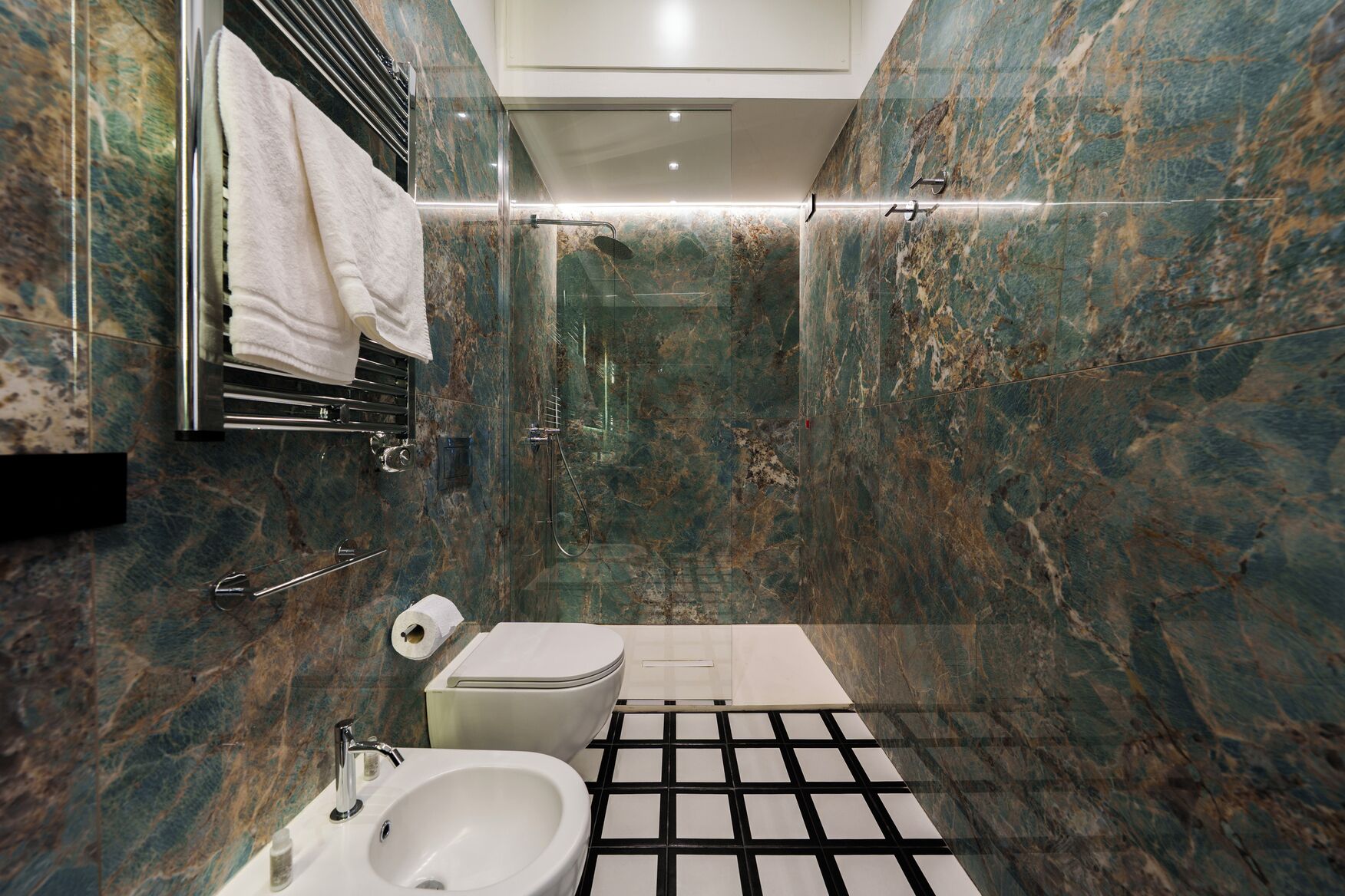 A modern bathroom with a marble wall, a white sink, a toilet, and a shower area.