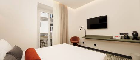 Ein Hotelzimmer mit Bett, einem an der Wand montierten Fernseher, einem kleinen Tisch mit Kaffeemaschine und einem Sessel.