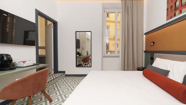 A hotel room with a bed, a desk, a chair, a mirror, and a window with curtains. - La Dimora del Corso 35 (Naples)