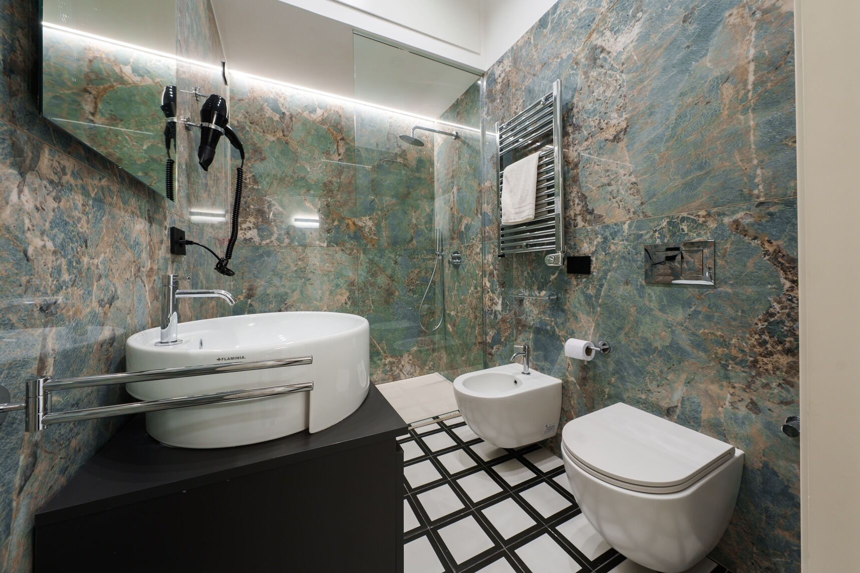 Un baño con un lavabo ovalado grande, un lavabo más pequeño, un inodoro y una ducha con mampara de vidrio.