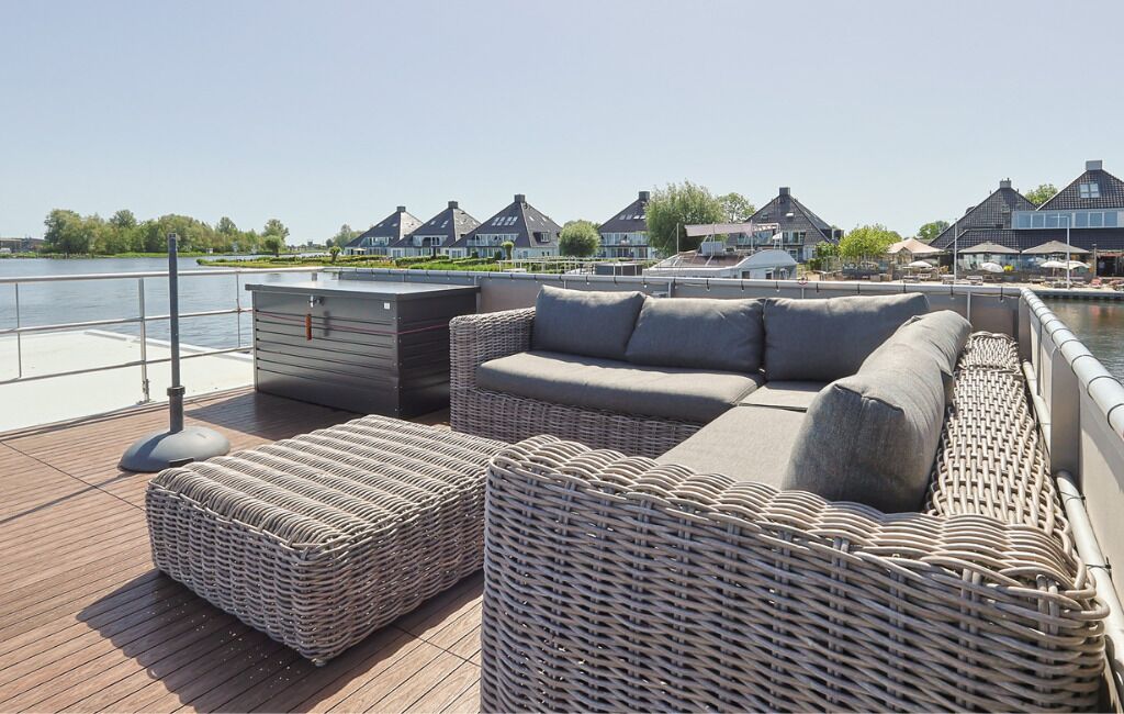 A deck with wicker furniture, a small storage unit, and a view of houses across the water.