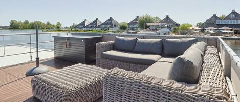 A deck with wicker furniture, a small storage unit, and a view of houses across the water.