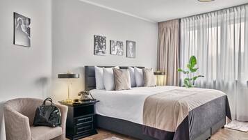 A bedroom with a bed, a nightstand, a chair, and a potted plant.