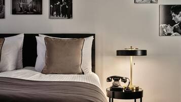 A neatly made bed with a black headboard, a bedside table with a classic telephone and a lamp, and a wall adorned with black-and-white photographs.