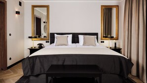 Une chambre d’hôtel avec un grand lit, deux tables de chevet, un banc et deux grands miroirs.