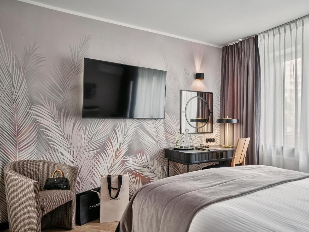 Een moderne hotelkamer met een groot bed, een flatscreen televisie aan de muur, een bureau met stoel, en een groot raam met gordijnen.